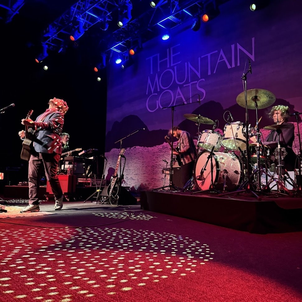 The Mountain Goats on stage at the Fillmore on December 10, 2025. From l-r: John Darnielle on vocals and guitar, Matt Douglas on various backing instruments including keyboards, Cameron Ralston on bass and Jon Wurster on drums.