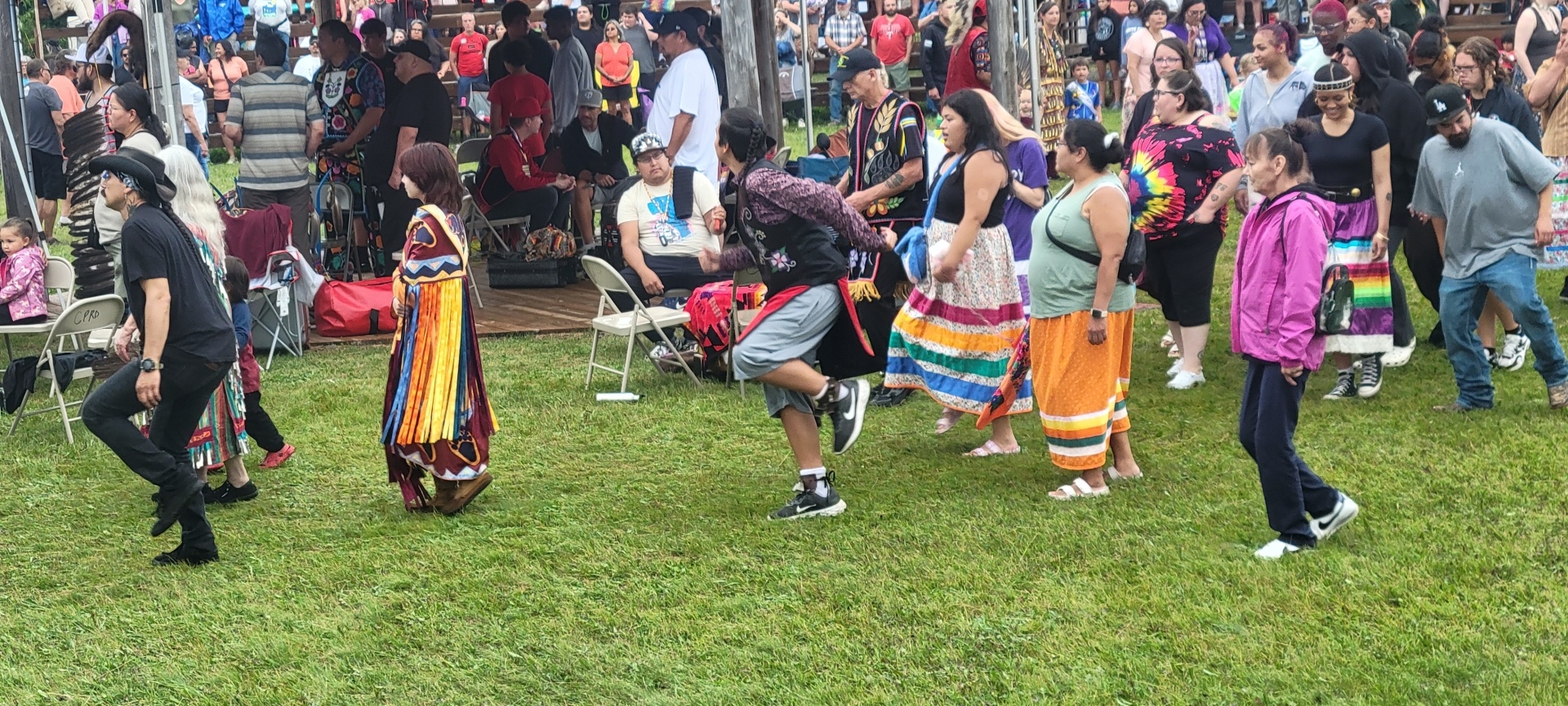 A Young Man dancing, surrounded by people in Jingle Dresses.