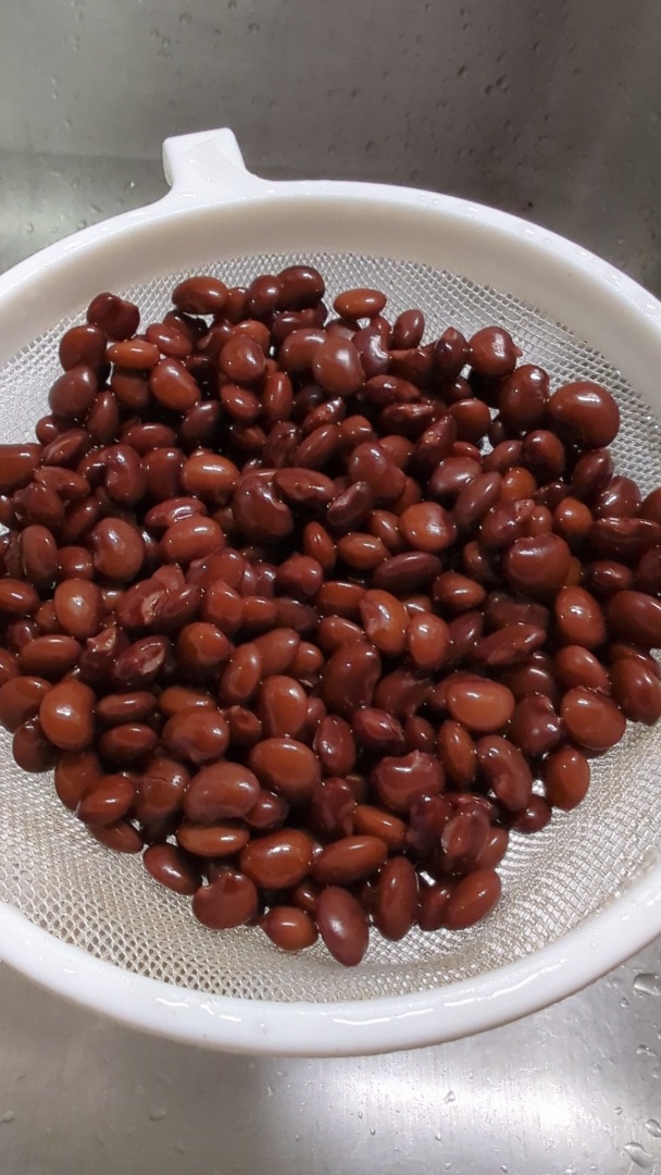 A small plastic strainer containing medium sized red beans. They're vaguely kidney shaped and colored, and mostly uniform. Some of the beans have burst slightly.