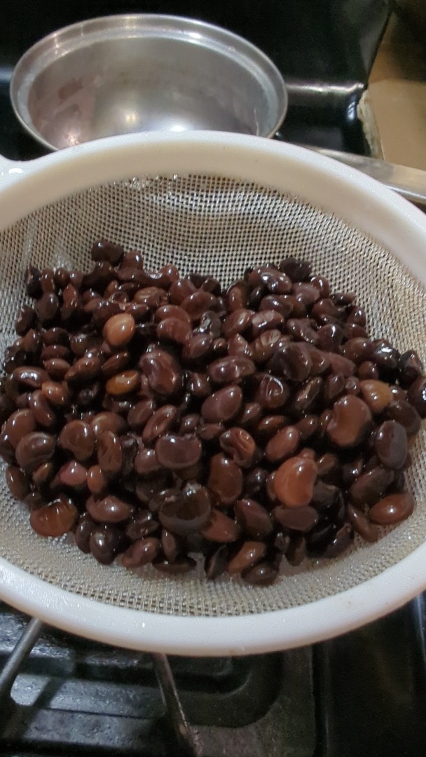 A small plastic strainer containing smallish, darkish beans. Their colors and sizes are quite variable but they're all fairy plump and they're all some shade of dark red.
